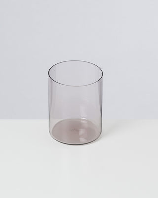 Ein durchsichtiges, zylindrisches Glasgefäß steht auf einer weißen Oberfläche vor neutralem Hintergrund.