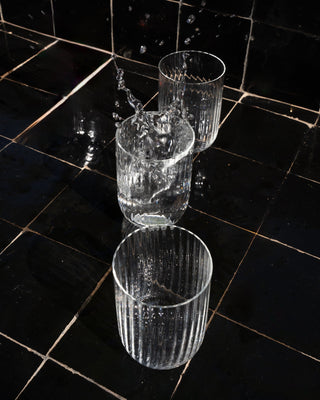 Drei leere Glasbecher auf schwarzen Fliesen, einer davon mit Wasserspritzern.