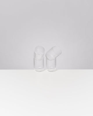 Zwei durchsichtige, geraffte Gläser, eines geneigt, auf einer weißen Fläche vor grauem Hintergrund.