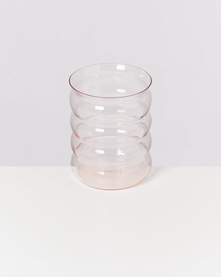 Ein transparentes Glas mit wellenförmigem Design steht auf einer weißen Oberfläche vor einem grauen Hintergrund.