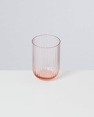 Ein geriffeltes, rosafarbenes Glas auf einer weißen Fläche vor einem grauen Hintergrund.