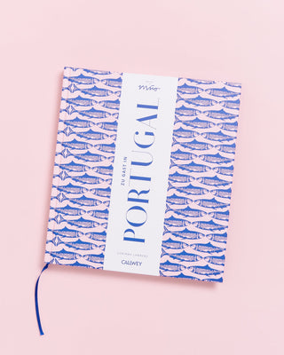 Kochbuch "Zu Gast in Portugal" mit blauem Sardinenmuster auf rosa Hintergrund.