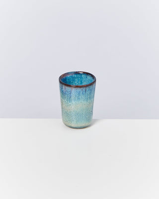 Keramikbecher mit blau-grünem Farbverlauf steht auf weißem Hintergrund.
