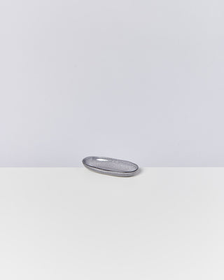 Graues, ovales Keramikschälchen auf einem weißen Tisch vor einem hellgrauen Hintergrund.