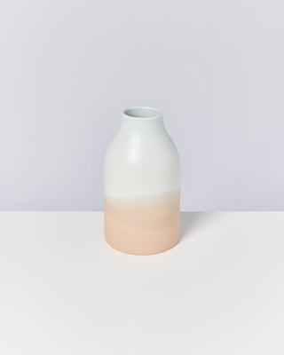 Minimalistische Vase in mattem Farbverlauf von Weiß nach Hellrosa, auf einem hellen Hintergrund stehend.