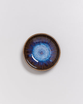 Keramikschale mit blau-braunem Design in der Mitte, auf weißem Hintergrund fotografiert.