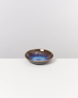 Keramikschale mit blauem Innenmuster auf weißem Tisch und grauem Hintergrund.