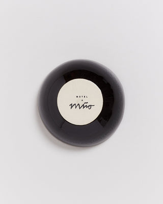 Runde schwarze Schale mit beigem Inneren und der Aufschrift "Motel a mio" auf heller Oberfläche.