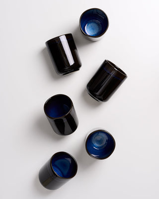 Sechs schwarze Keramikbecher mit blauer Innenseite liegen auf weißem Hintergrund.