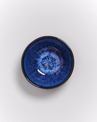 Eine Keramikschale mit blauer Glasur und einem abstrakten Muster auf hellem Hintergrund.