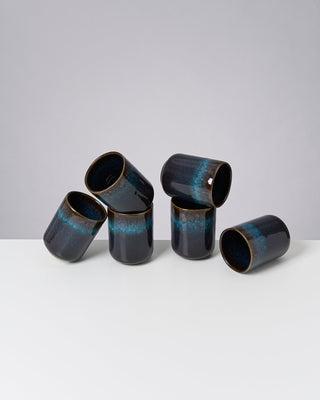Sechs dunkelblaue Keramikbecher mit hellblauem Streifen auf einer weißen Fläche vor grauem Hintergrund.
