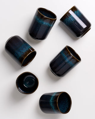 Sechs schwarze Keramikbecher mit blaugrüner Glasur sind auf einem weißen Hintergrund verteilt.