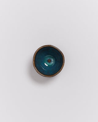 Kleine, runde Schale mit blau-grüner Glasur und braunem Rand auf weißem Hintergrund.