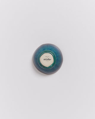 Runder, blauer Keramikknopf auf weißem Hintergrund mit einer Signatur in der Mitte.