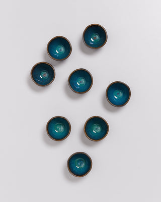 Acht kleine Schalen mit blauer Glasur sind auf einem weißen Untergrund angeordnet.