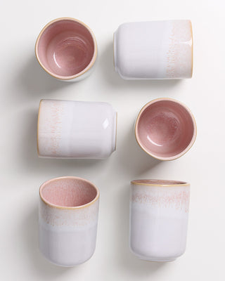 Sechs Keramikbecher in rosa und weiß auf hellem Hintergrund, teilweise liegend, teilweise stehend.