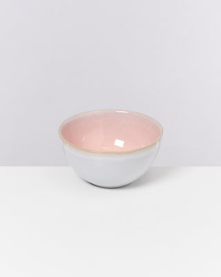 Eine Keramikschüssel mit rosa Innen- und grauer Außenseite steht auf einem weißen Tisch vor einem hellgrauen Hintergrund.