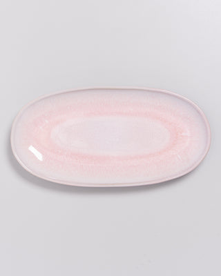 Ein ovaler Teller in zartem Rosa mit glatter Oberfläche auf einem weißen Hintergrund.