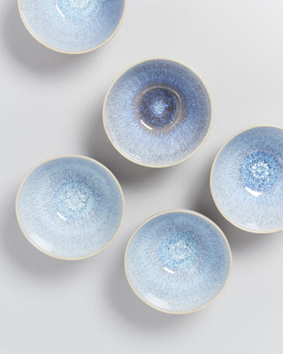 Fünf runde Schalen mit blauer, gesprenkelter Glasur auf grauem Hintergrund.