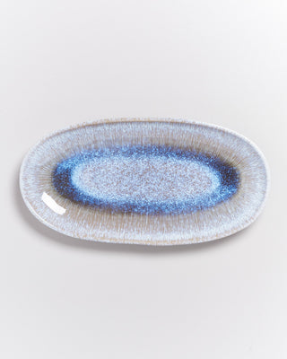 Ovaler Teller mit blauem und beigem Muster auf weißem Hintergrund.