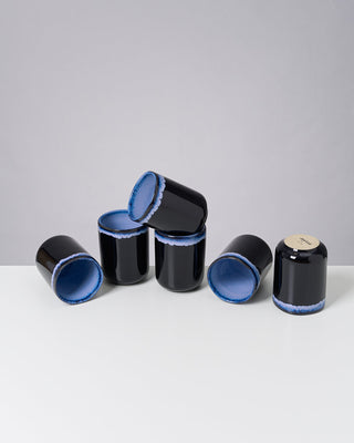 Sechs schwarze Keramiktassen mit blauer Innenfläche auf einem weißen Tisch vor grauem Hintergrund.