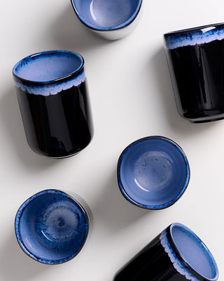 Sechs blau-glasierte Keramikbecher auf weißem Hintergrund, teilweise von oben sichtbar.