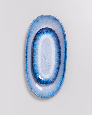 Ovale, blau-weiß gemusterte Keramikplatte mit glänzender Oberfläche auf grauem Hintergrund.
