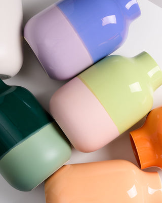 Mehrere bunte Vasen in Pastellfarben liegen auf einer weißen Oberfläche.