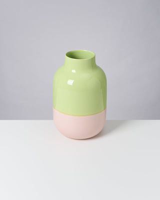 Zweifarbige Vase in Hellgrün und Rosa steht auf einem weißen Tisch vor grauem Hintergrund.
