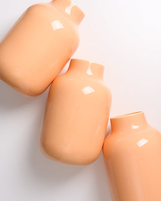 Drei orangefarbene Vasen liegen schräg nebeneinander auf einer weißen Oberfläche.