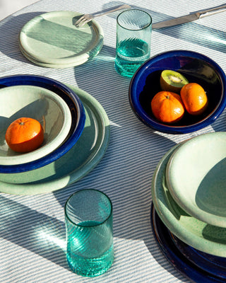 Ein gedeckter Tisch mit grünen und blauen Tellern, Gläsern und Schalen, gefüllt mit Mandarinen und einer Kiwi.