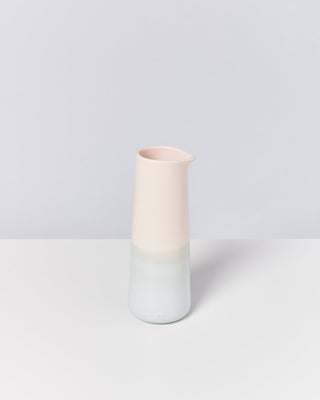 Schlanker, zweifarbiger Krug in Pastellrosa und Blau steht auf einem weißen Tisch vor einem grauen Hintergrund.