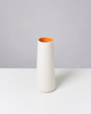 Weiße Vase mit orangefarbenem Inneren steht auf einem weißen Tisch vor grauem Hintergrund.