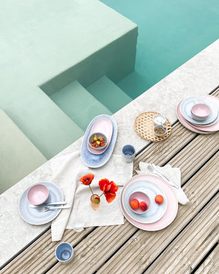 Ein gedeckter Tisch mit buntem Geschirr und Blumen am Rand eines Pools.