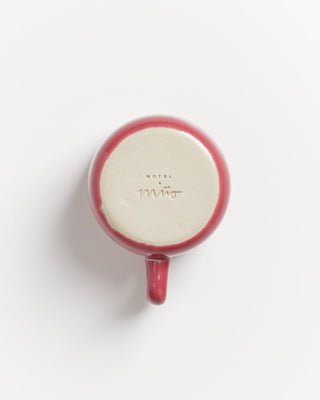 Rote Tasse von unten, auf der der Name "Mio Hotel" eingeprägt ist, auf weißem Hintergrund.