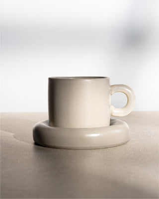 Weiße Keramiktasse mit passender Untertasse auf einer hellen Oberfläche.