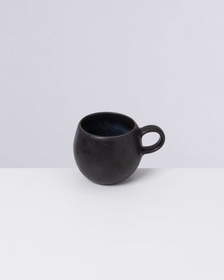 Schwarze, runde Tasse mit Henkel auf einer grauen Oberfläche vor hellem Hintergrund.