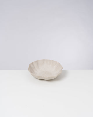 Beige keramische Schale mit welligem Rand auf weißer Oberfläche vor neutralem Hintergrund.