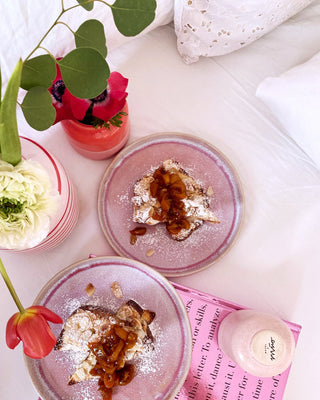 Zwei Teller mit Dessert und Karamell auf einem Bett, umgeben von Blumen in Vasen.